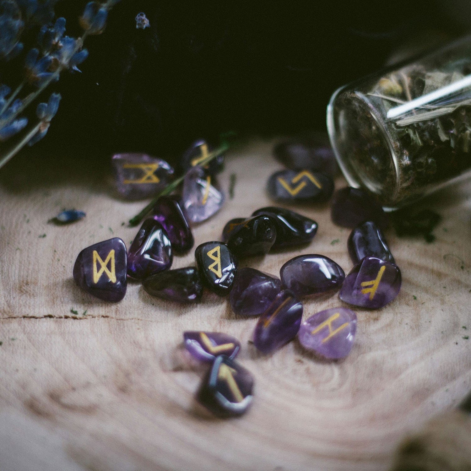 Purple rune stones laid out on wood with herbs in background