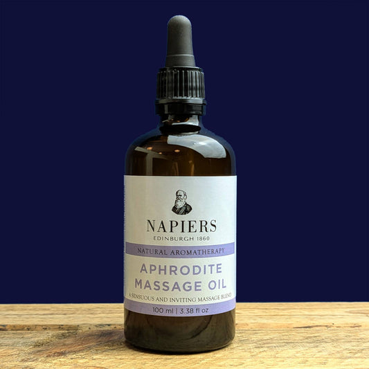 Bottle of Napiers Aphrodite Massage Oil on a wooden surface with a dark blue background
