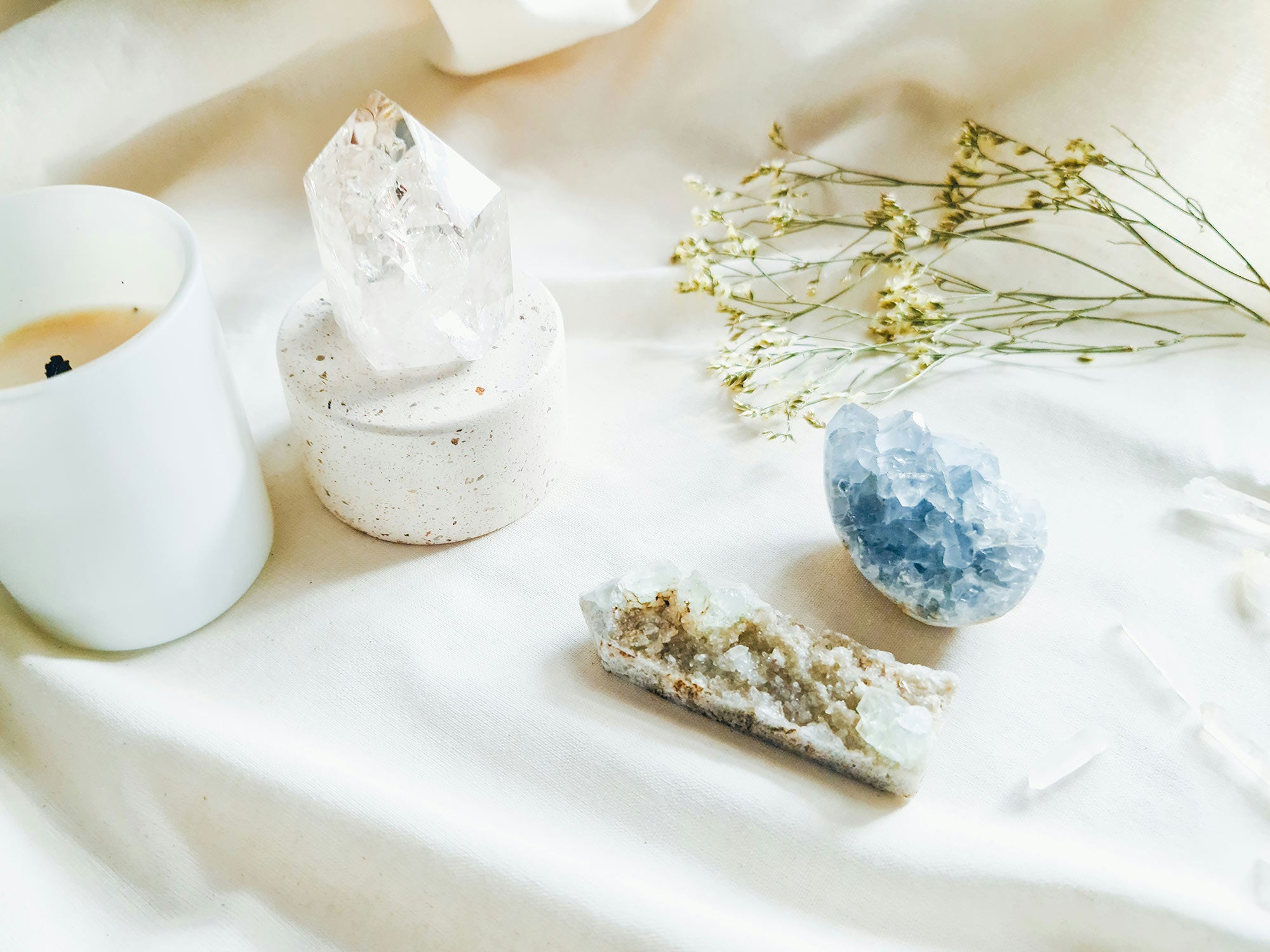 Candle, decorative crystals, and dried flowers on a white fabric background