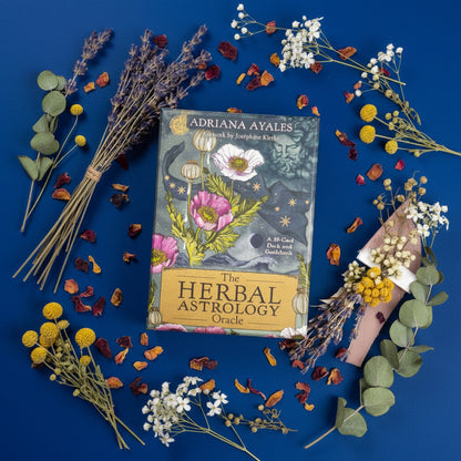 The Herbal Astrology Oracle deck by Adriana Ayales on a blue background with dried herbs.