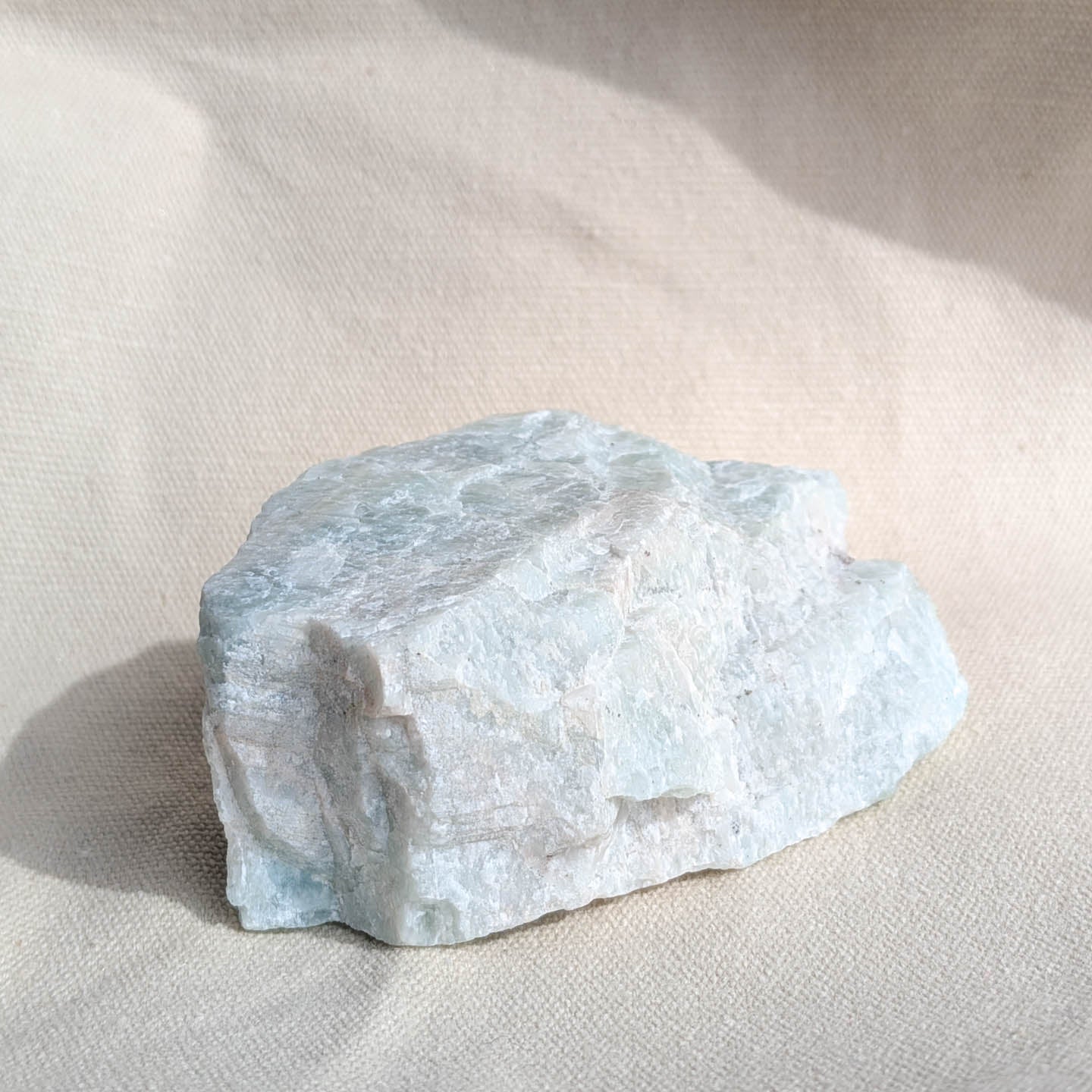 Large raw amazonite crystal on a light beige fabric background