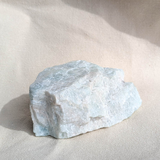 Large raw amazonite crystal on a light beige fabric background