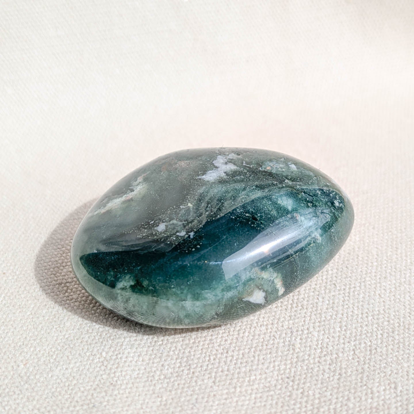 Marbled green and gray moss agate crystal on a beige fabric background