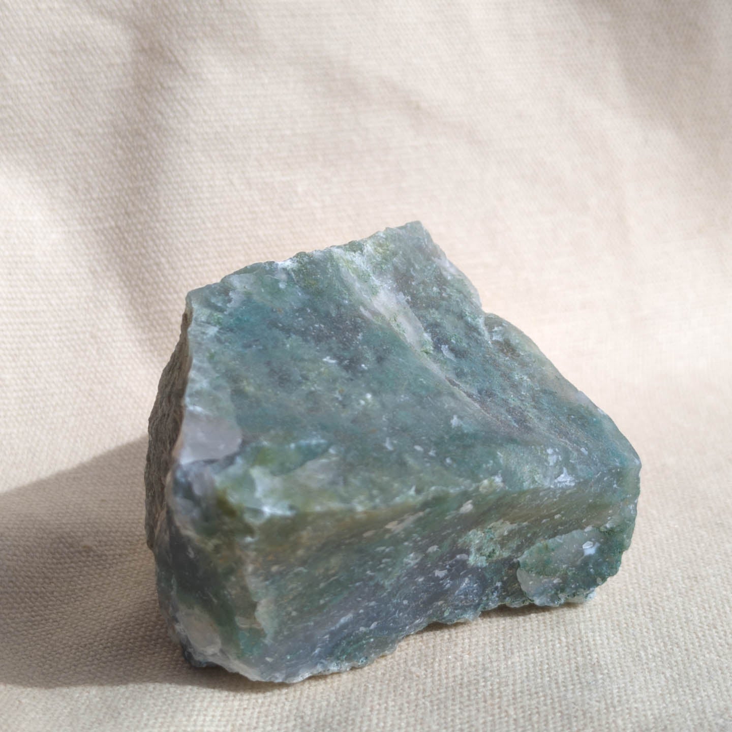 Raw green moss agate crystal on a beige fabric background