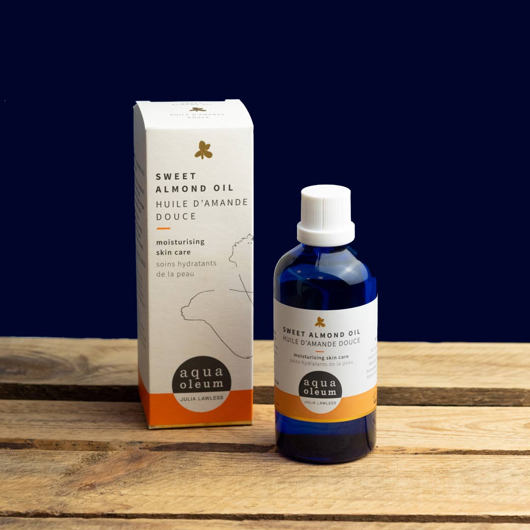 Bottle and box of aqua oleum sweet almond oil on a wooden surface with a dark blue background