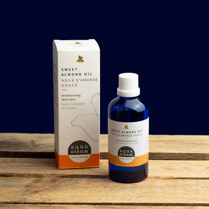 Bottle and box of aqua oleum sweet almond oil on a wooden surface with a dark blue background