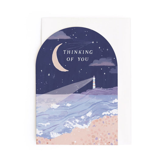 Greeting card with a lighthouse, moon, and stars on a night sky background.