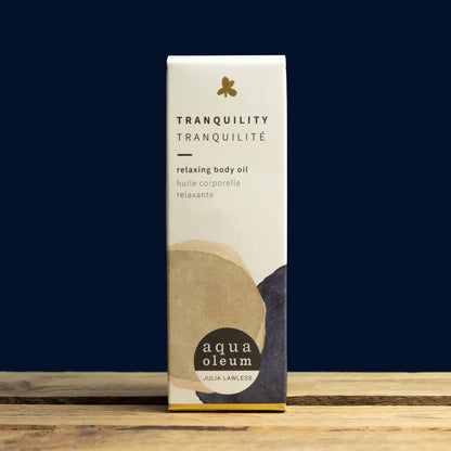 Box of Tranquility relaxing body oil by aqua oleum on a wooden surface with a dark blue background