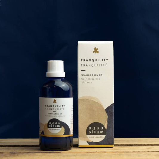 Aqua Oleum Tranquility relaxing body oil bottle and packaging on a wooden surface with a dark background