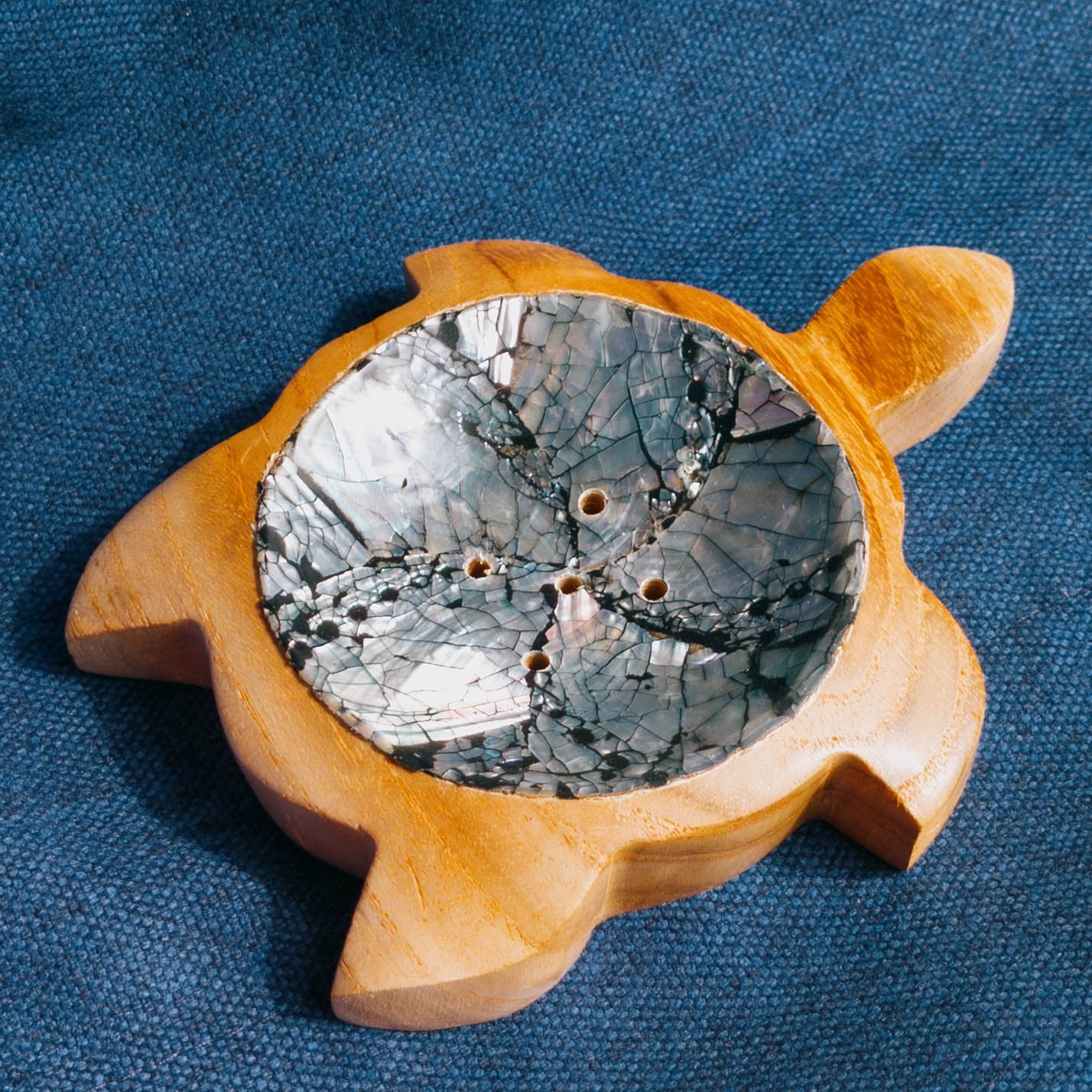 Wooden turtle soap dish with a textured stone inset on a blue fabric background
