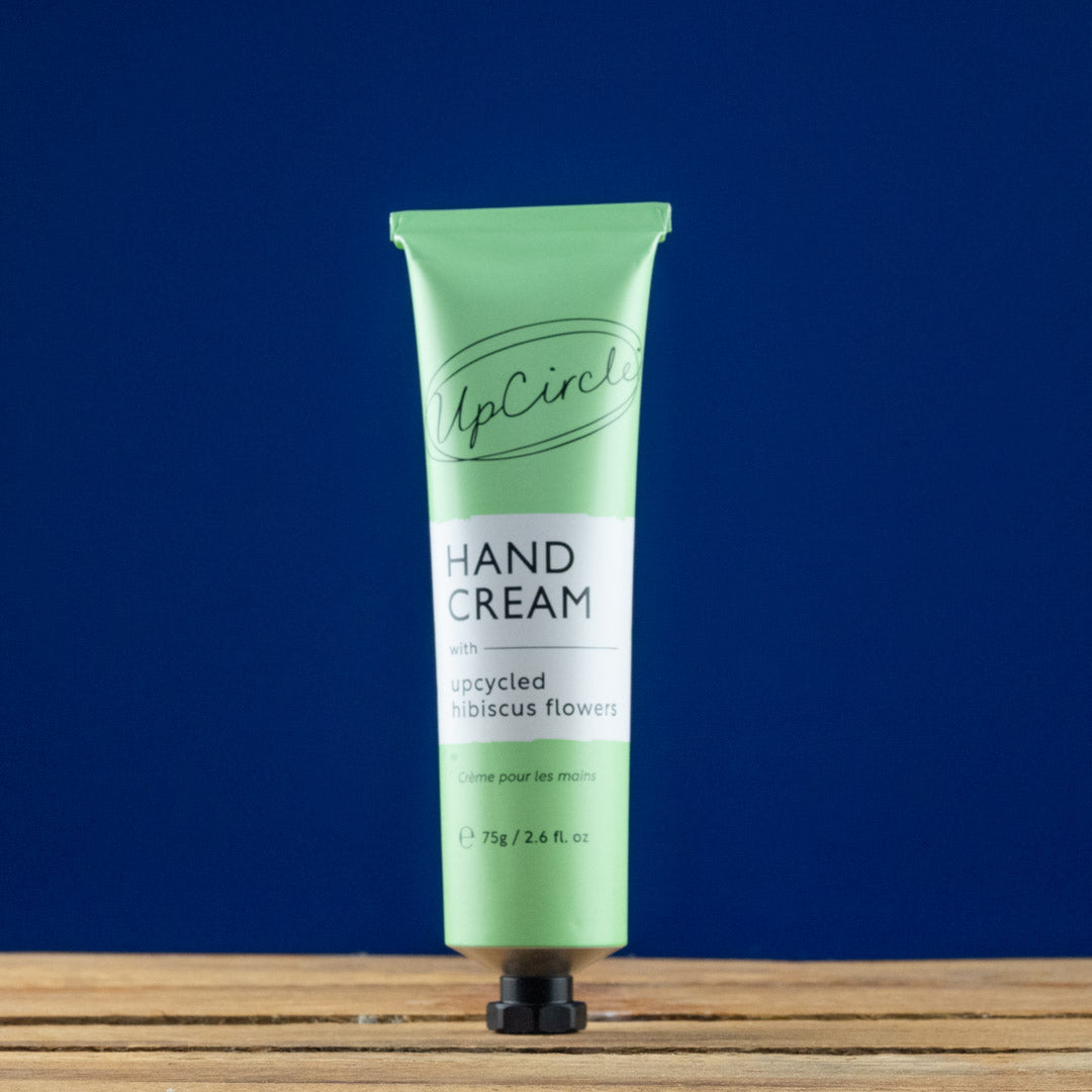 Green hand cream tube labeled 'UpCircle' on a wooden surface with a blue background
