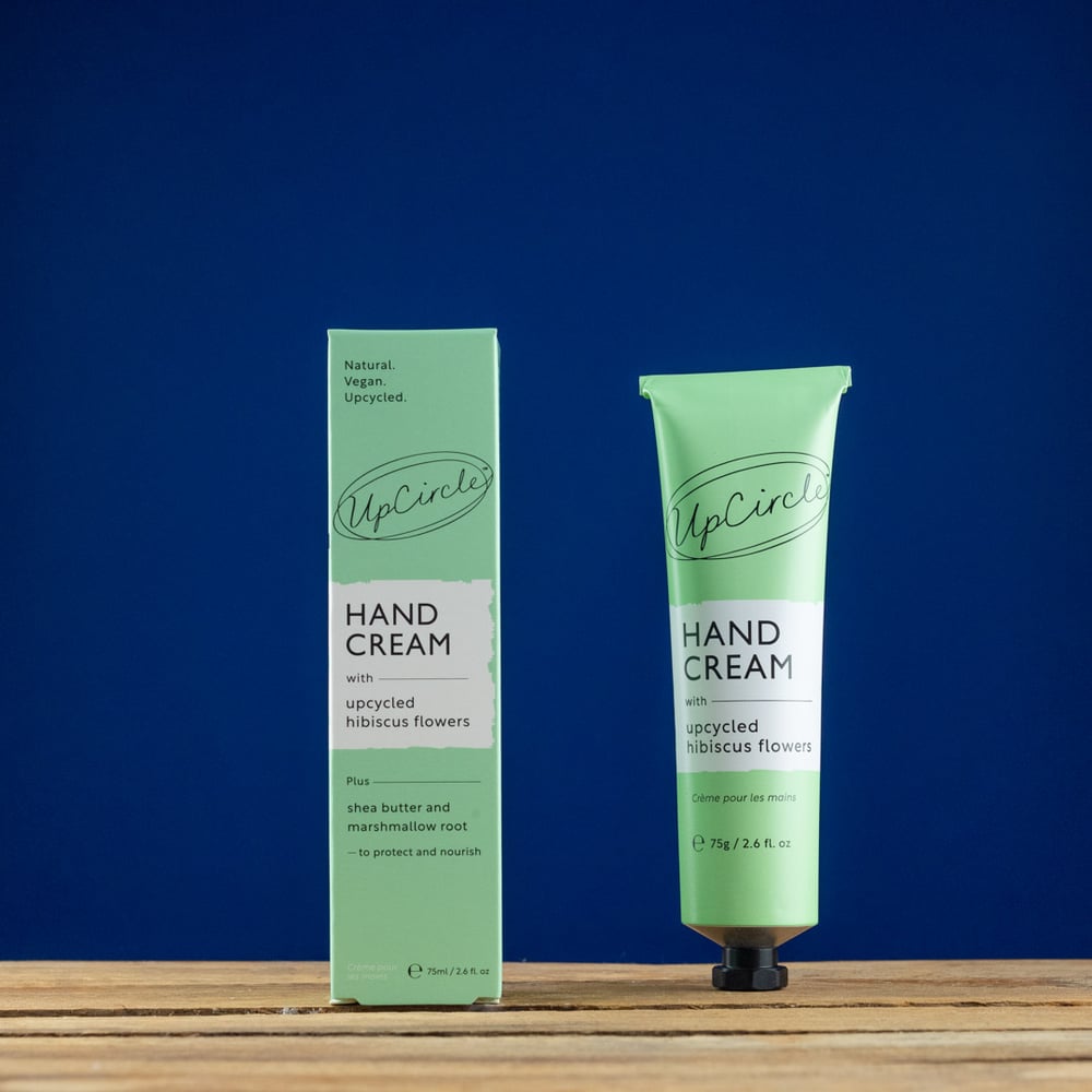 Green hand cream tube and packaging on a wooden surface with a blue background