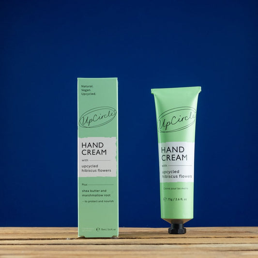 Green hand cream tube and packaging on a wooden surface with a blue background